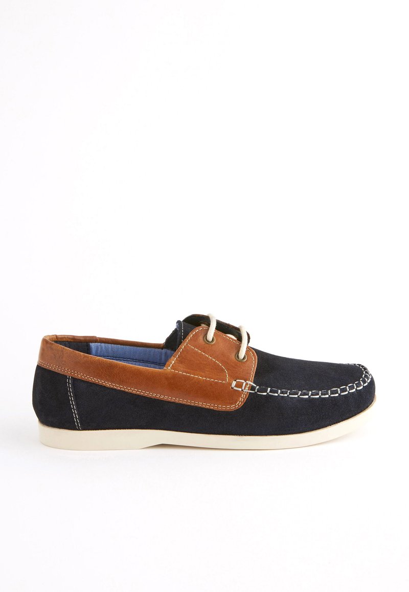 Scarpa da barca blu in suede con accenti in pelle marrone, cuciture bianche lungo la parte superiore e una suola bassa color crema.