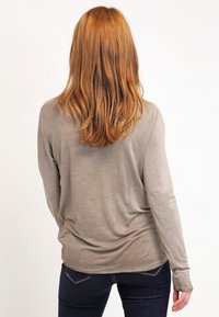 Camicia taupe a maniche lunghe con una morbida texture, vestibilità rilassata e dettaglio arricciato sul retro, abbinata a jeans blu scuro.