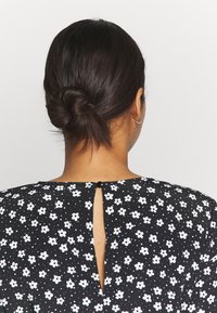 Musta kukallinen mekko, jossa on valkoisia kukkia, avainreikäleikkauksella ja napituksen sulkijalla takana. Silkkinen, kevyt kangas.