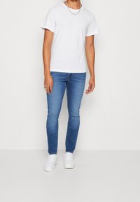 Camiseta de algodón blanca de manga corta, combinada con jeans ajustados azules y zapatillas blancas. Presenta un diseño simple con un cuello redondo.