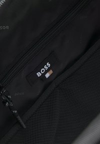 Interno di una borsa in nylon nero con una tasca con zip, un'etichetta con il marchio "BOSS" e un compartimento in rete per l'organizzazione.