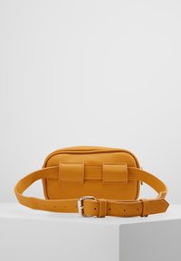 Sac bandoulière en cuir jaune moutarde à surface texturée, forme rectangulaire, deux brides avant et une ceinture à boucle réglable.