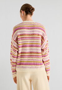 Pull en tricot avec des rayures horizontales roses, dorées et crème. Coupe ample avec des poignets et un ourlet côtelés ; le motif texturé apporte un intérêt visuel.