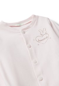 Bodysuit de algodón de color rosa claro para bebé, con cierres de botones, que presenta un diseño de conejito impreso dentro de un corazón y la marca "benetton."