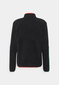 Black fleece jacket with a high collar, long sleeves, green side panels, and red trim on collar and hem, shown from the back.