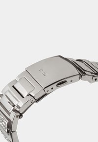 Sudraba nerūsējošā tērauda pulksteņa rokassprādze ar pulētām saiknēm, sarežģītiem izstrādājumiem un drošu sprādzi ar iegravētu zīmola logo.