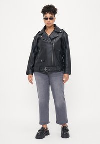 Black faux leather biker jacket with silver zippers, belted waist, and side pockets. Paired with gray straight-leg jeans and black platform clogs.
