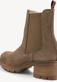 Bottine en suede marron avec panneau élastique texturé sur les côtés, talon empilé et languette. Des détails de couture subtils viennent mettre en valeur le design.