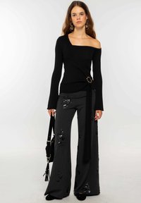 Top negro de punto sin hombros con un diseño envolvente y un cinturón con acentos dorados, combinado con pantalones de pierna ancha grises con lentejuelas florecidas. Se incluye un bolso negro.
