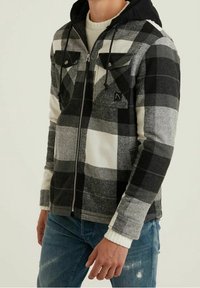 Czarna i biała kurtka z flaneli w kratę z kapturem, zamkiem z przodu i dwoma kieszeniami na piersiach, o miękkiej fakturze i kontrastowych rękawach.