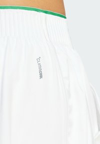 Witte sportshorts met een groene elastische tailleband, lichte stof en een zilveren "climacool" logo aan de zijkant.