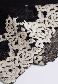 Tela de encaje negra con un intrincado patrón floral crema y bordes en forma de concha, que muestra un bordado detallado y una textura transparente.