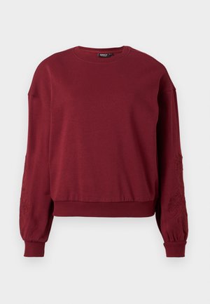 Felpa a maniche lunghe color bordeaux con colletto rotondo, polsini e orlo a coste, caratterizzata da un delicato ricamo floreale sulle maniche.