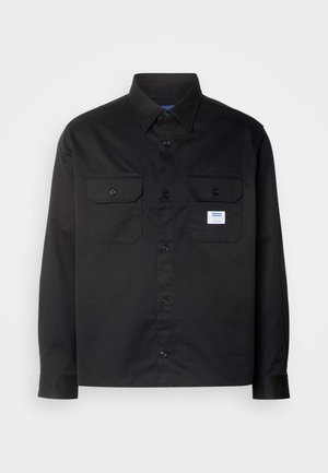 Chemise noire à manches longues en coton. Dotée d'une fermeture à boutons, de deux poches poitrine et d'une petite étiquette logo sur la poche gauche.