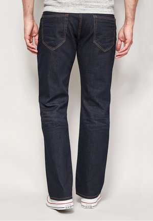 Donkerblauwe denim jeans met een recht model, zichtbare stiksels en vier achterzakken, gecombineerd met witte sneakers.