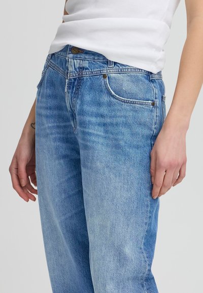 Gai zila džinsu auduma bikses ar brīvu piegulšanu, piecu kabatu dizainu un redzamām šuvēm. Audumam ir nedaudz nolietots raksts.