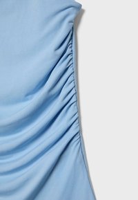 Světlounce modrá látka s vertikálním řasením podél jedné strany na jednobarevném světle šedém pozadí.