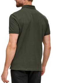 Polo shirt vert foncé avec col, manches courtes et fentes sur les côtés. Fabriqué à partir d'un tissu lisse et texturé, offrant une coupe classique.