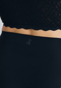 Black cotton briefs with a smooth texture and logo detail. The waistband features a scalloped edge, complementing the fitted design.
