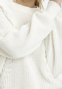 Biała dzianinowa sweter o grubej strukturze, w luźnym kroju, z detalami w warkocz wzdłuż boku, z ściągaczami na mankietach i dekolcie.