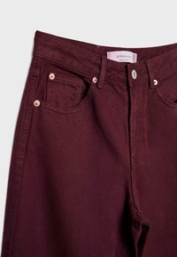 Pantalon en denim bordeaux avec bouton frontal et rivets, doté de poches avant et de passants pour ceinture, taille 36 de la marque Stradivarius.