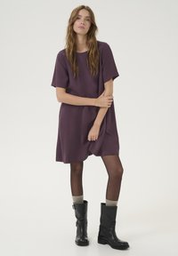 Robe violette à manches courtes avec un col rond, une coupe fluide et une coupe décontractée, associée à des bottes noires montantes et des chaussettes grises à motifs.