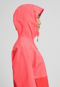 Veste à capuche corail vif avec une texture lisse. Comprend un cordon de serrage ajustable à la capuche et un design élégant et ajusté.