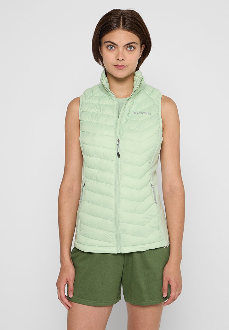 Gilet matelassé sans manches vert clair avec fermeture éclair à l'avant, motif en chevrons, poches latérales et col pliable, associé à un short vert olive.