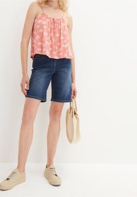 Rosa blommig tanktop med spaghettiband, denimshorts och beige sneakers. Inkluderar en vävd beige handväska. Enkel, avslappnad sommaroutfit.