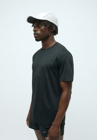 T-shirt noir avec un col rond, des manches courtes et des détails discrets sur le côté. Associé à une casquette grise clair avec un panneau texturé.