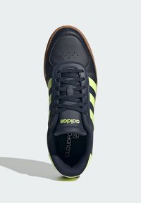 Navy leather sneaker with three neon green stripes, black laces, and a brown rubber sole. Features perforated toe and cushioned collar.