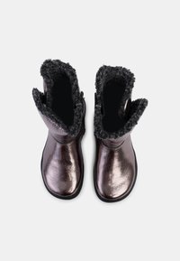 Botas tobilleras en bronce metálico con puños de pelo sintético, textura suave, punta redondeada y cremalleras laterales para facilitar el uso. Suelas de goma negra.