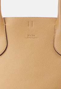 Tan läder tote-väska med en strukturerad yta. Har två handtag och präglad logotyp "Polo by Ralph Lauren" på framsidan. Enkel design.