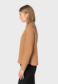 Camelfarvet sweater med lange ærmer, blød tekstur, rund krave og sidesømmer, båret med sorte bukser. Sidens view viser en afslappet pasform.