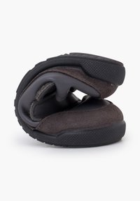 Scarpa pieghevole con tomaia in suede marrone scuro e suola in gomma flessibile. Presenta un design semplice con interno imbottito e forma arrotondata.