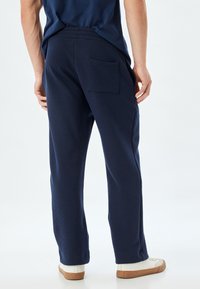 Pantalones de canalé azul marino con un ajuste relajado, que cuentan con un único bolsillo trasero y cintura elástica. Combinados con zapatillas blancas informales.