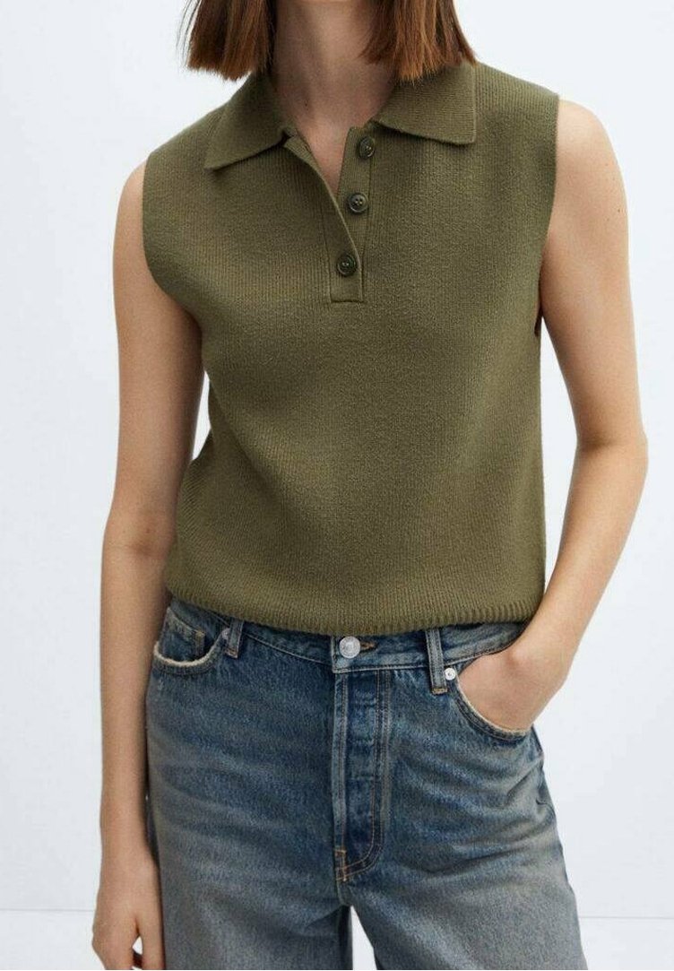 Haut polo en maille vert olive sans manches avec trois boutons, porté rentré dans un jean bleu taille haute, une main dans la poche.