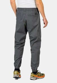 Graue Jogginghose mit elastischem Bund, seitlichen und hinteren Taschen, schmal zulaufendem Saum, kombiniert mit grünen und orangefarbenen Sportschuhen.