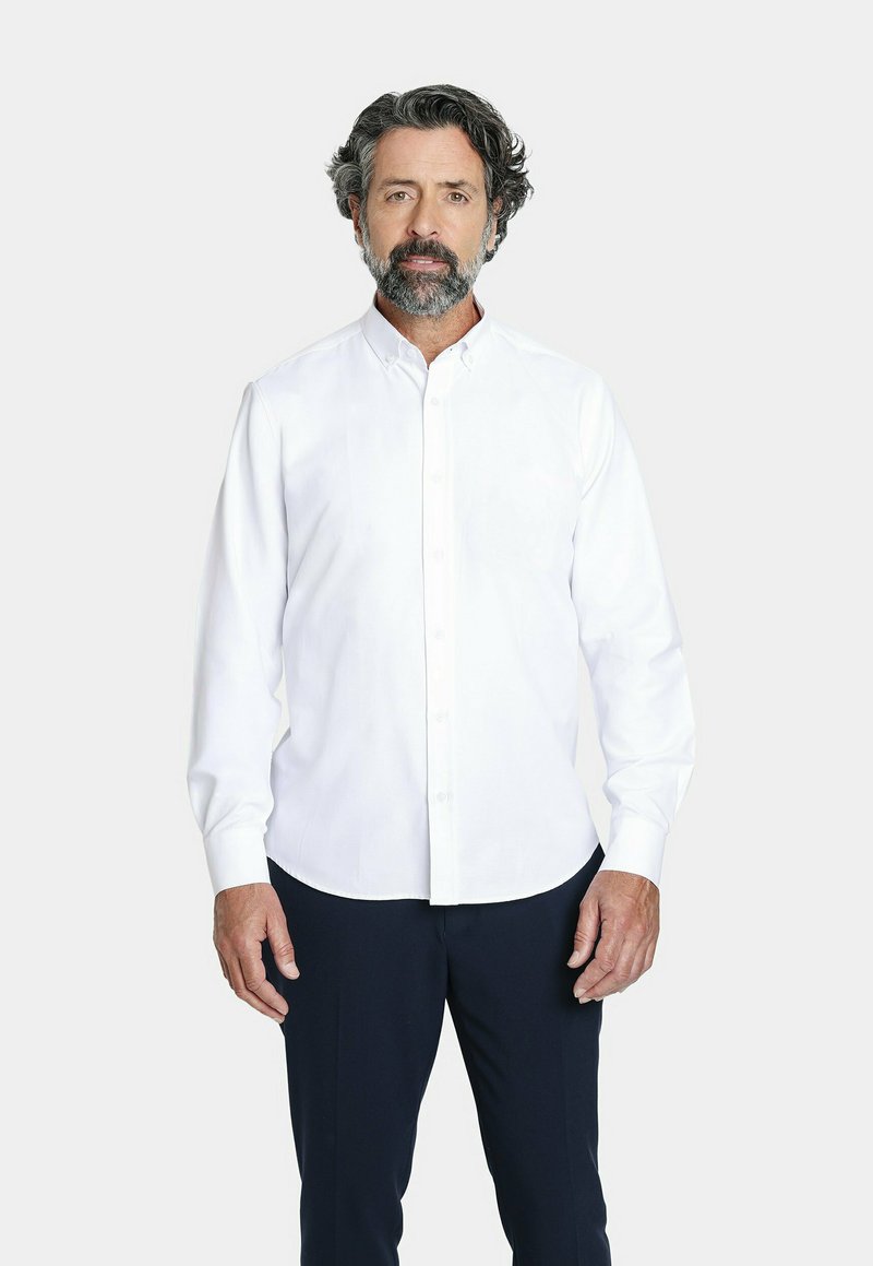 Camisa blanca de manga larga con botones y cuello puntiagudo, con un diseño liso y textura suave, combinada con pantalones azul marino.