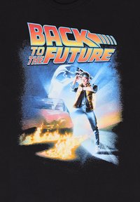 T-shirt nera con una grafica colorata di "Ritorno al Futuro". Il design include un'auto, fiamme e un personaggio con una giacca di jeans e uno skateboard.