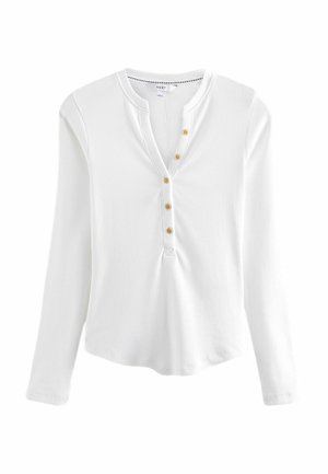 Chemise blanche à manches longues côtelée avec encolure henley et cinq petits boutons beiges alignés au centre devant.
