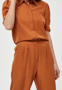 Rust orange shirt with a classic collar and short rolled sleeves, paired with matching pants featuring a subtle textured pattern.