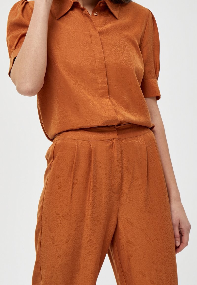 Rust orange shirt with a classic collar and short rolled sleeves, paired with matching pants featuring a subtle textured pattern.