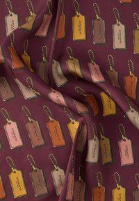 Veininpunane kangas, millel on korduv mustriga pagasimärgid erinevates värvides: pruun, oranž, kreemikas ja roosa, igaühel helmestega kett.