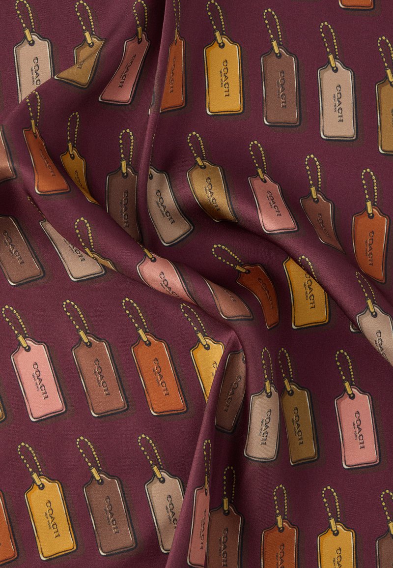 Tessuto color amaranto con un motivo ripetuto di etichette per bagagli in vari colori: marrone, arancione, crema e rosa, ciascuna con una catenina di perline.