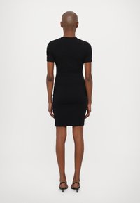 Juoda prigludusi suknelė su trumpomis rankovėmis, besiūlė konstrukcija, iki kelių, ir švelni tekstūra. Vaizdas iš nugaros, atskleidžiantis stilingą siluetą.