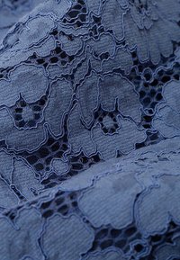 Tela de encaje en azul marino con patrones florales, tejido abierto, superficie texturada y costuras detalladas que crean profundidad.