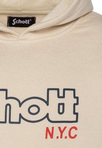 Sudadera beige de tejido suave con un logo azul "schott" y letras rojas "N.Y.C." en el frente, con capucha ajustable.
