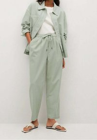 Světlá zelená, volně střižená bunda a kalhoty vyrobené z jemného materiálu. Bunda má límec a jednu náprsní kapsu; kalhoty mají elastický pas a šňůrku.