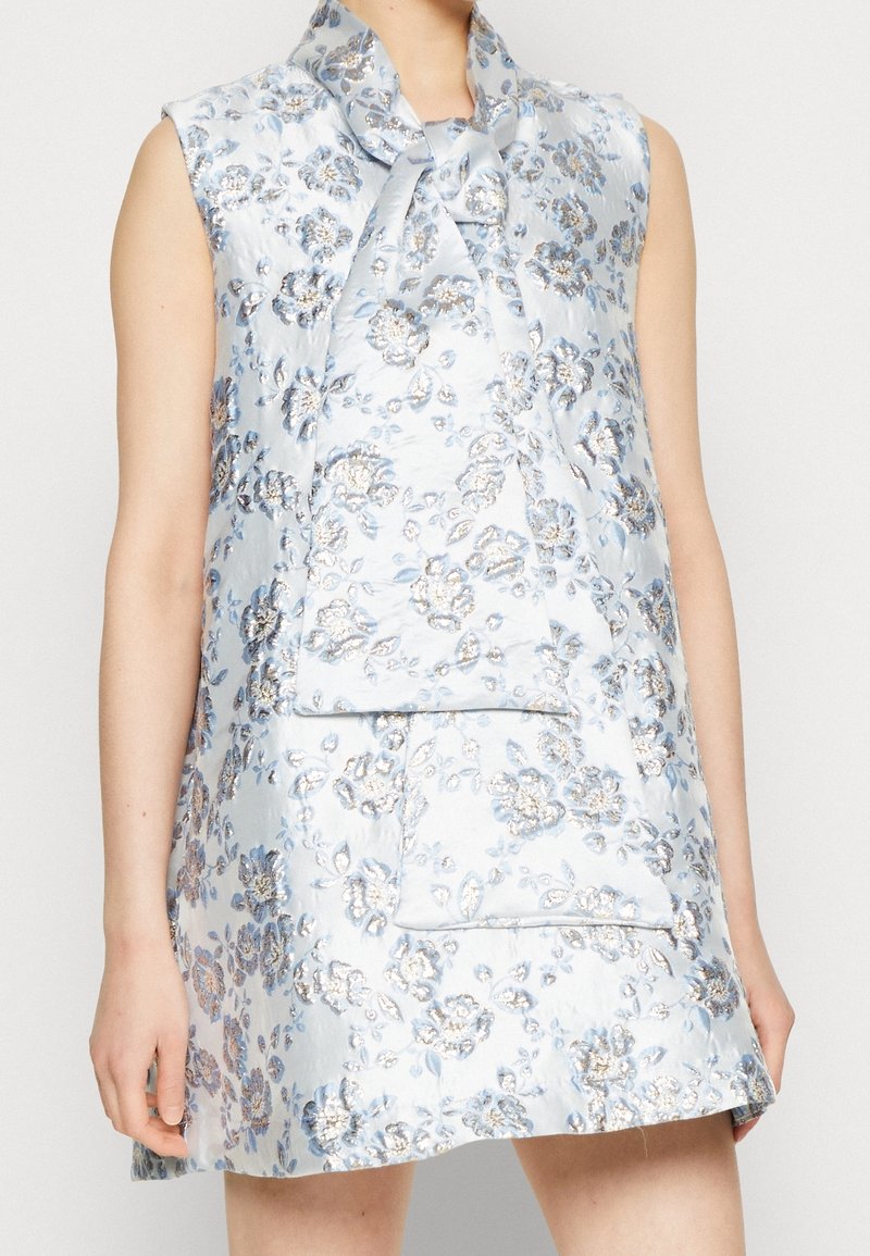 Vaaleansininen ilman hihoja oleva mekko kukkakuosisena, jossa on kimaltavia yksityiskohtia. Mekossa on leveä kaulus ja suorakulmainen tasku edessä.